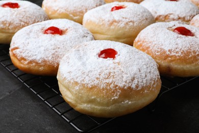 Photo of Many delicious donuts with jelly and powdered sugar on black table, closeup
