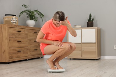 Photo of Woman in sportswear standing on floor scales at home