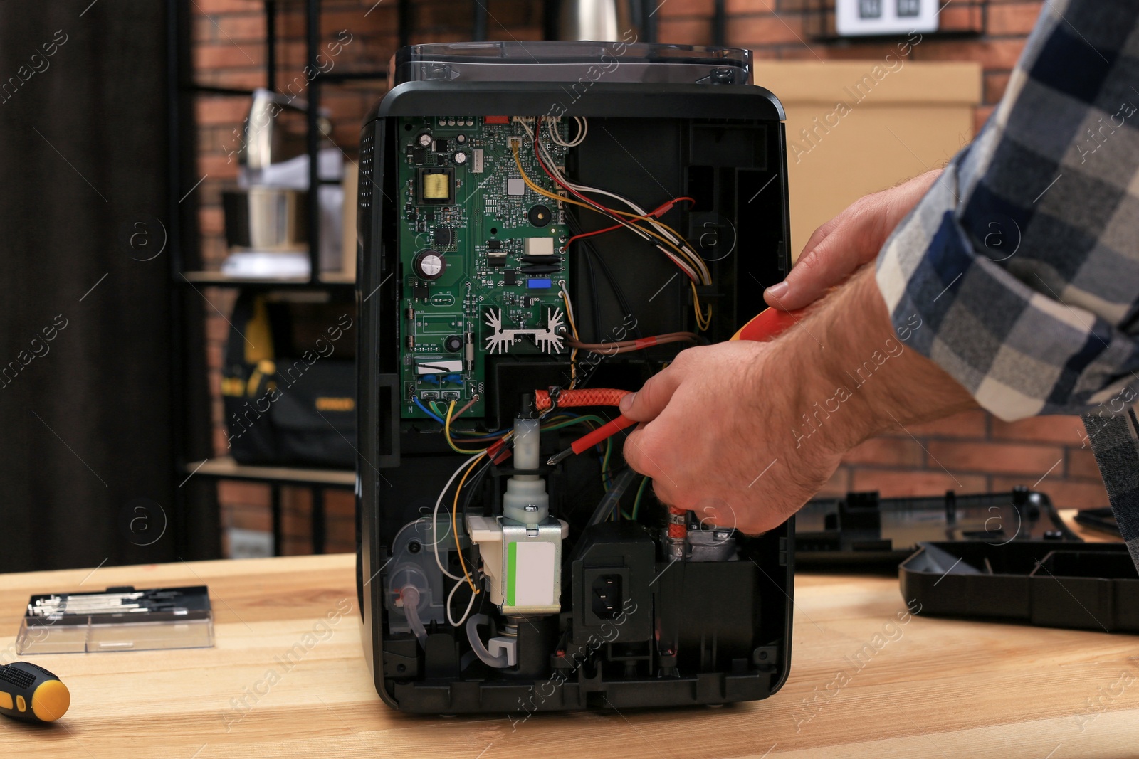 Photo of Man with screwdriver fixing coffee machine at table indoors, closeup