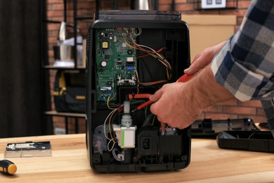 Photo of Man with screwdriver fixing coffee machine at table indoors, closeup