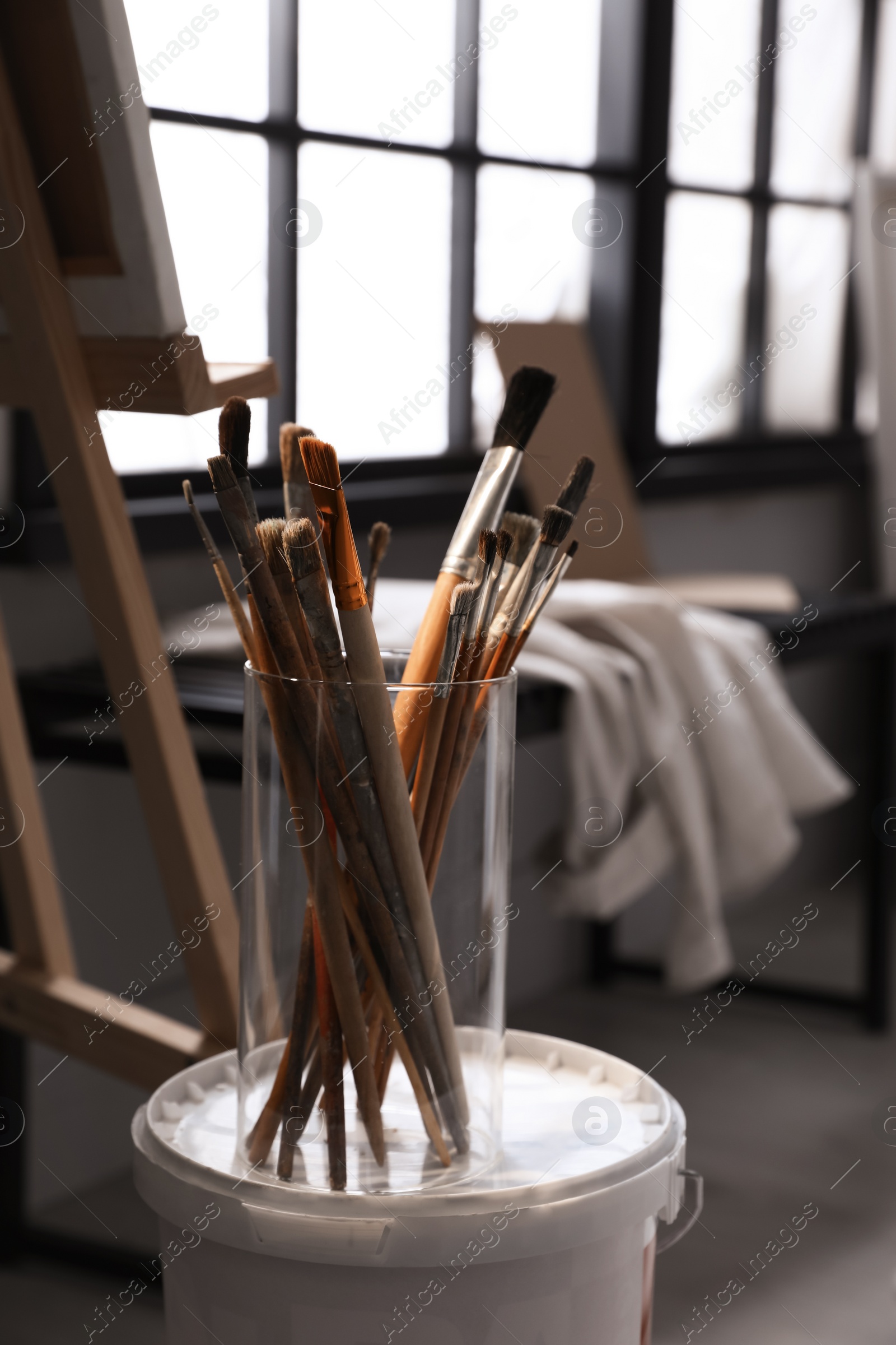 Photo of Holder with different brushes on bucket of paint in artist's studio