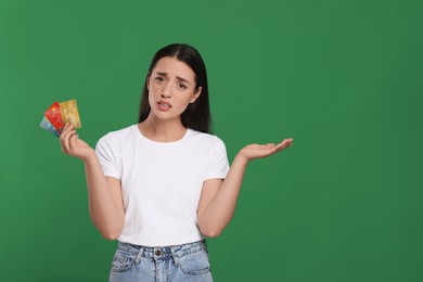 Photo of Confused woman with credit cards on green background, space for text. Debt problem