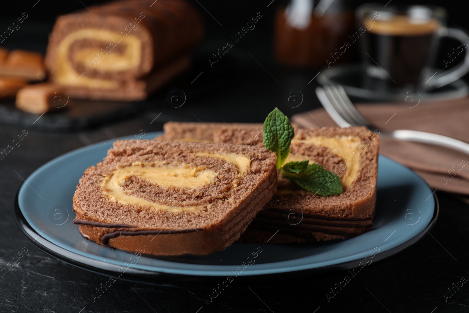 Photo of Tasty chocolate cake roll with cream on black table, closeup