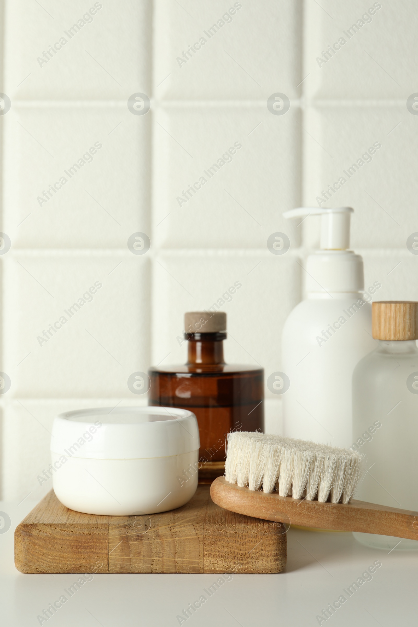 Photo of Bath accessories. Personal care products and wooden brush on white table near tiled wall