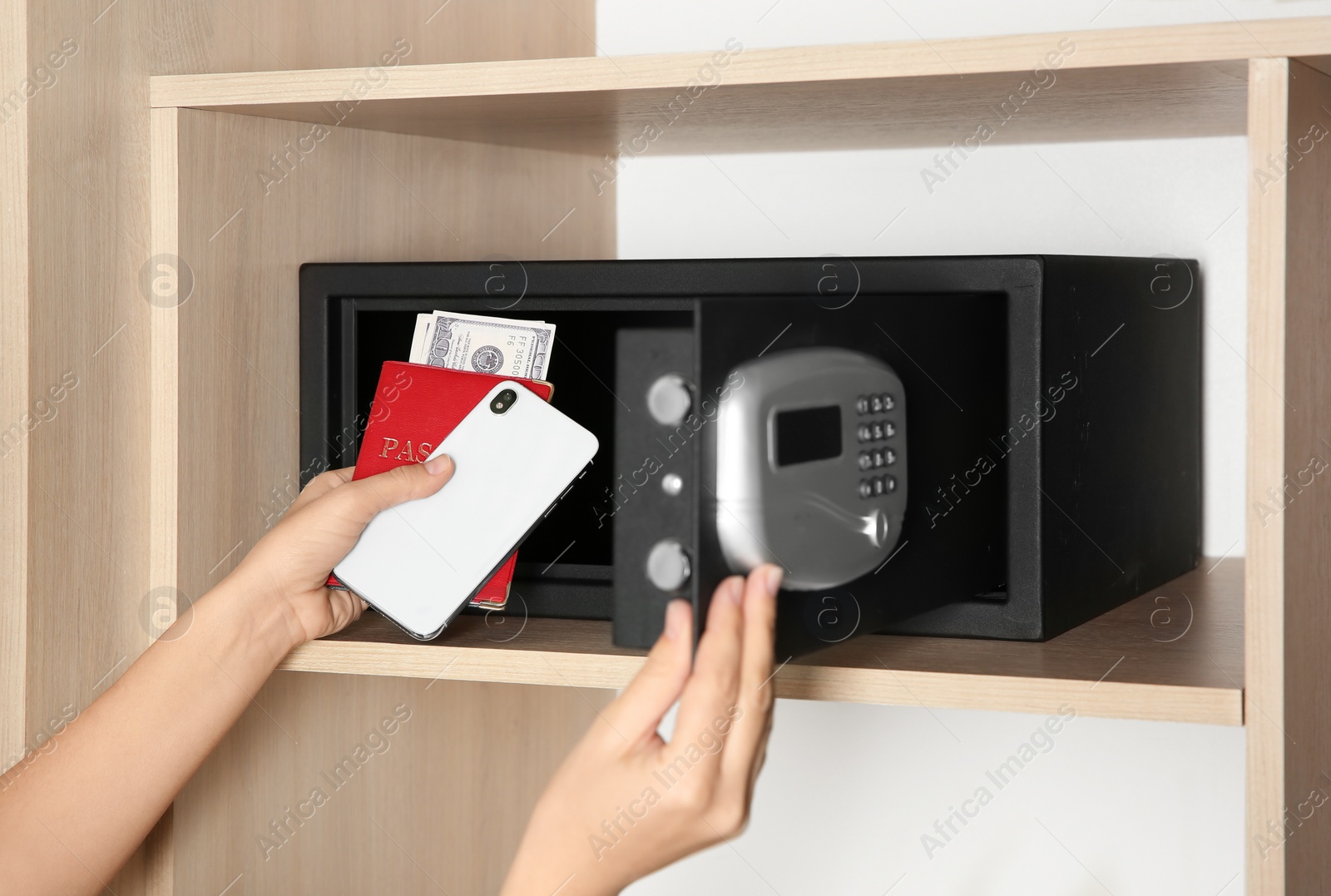 Photo of Woman putting smartphone, passport and money into steel safe, closeup