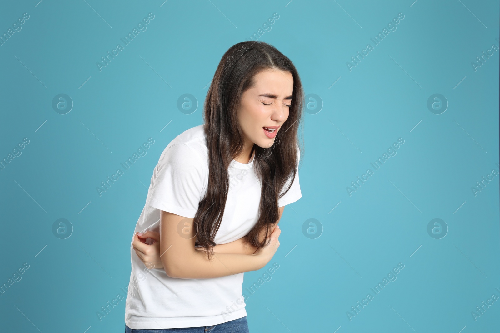 Photo of Young woman suffering from stomach ache on light blue background. Food poisoning