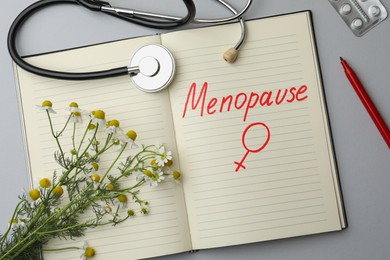 Photo of Flat lay composition of notebook with word Menopause and female gender sign on light grey background