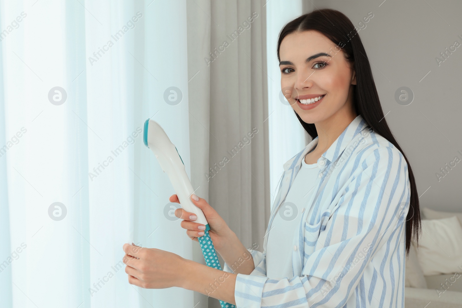 Photo of Woman steaming curtain near window at home