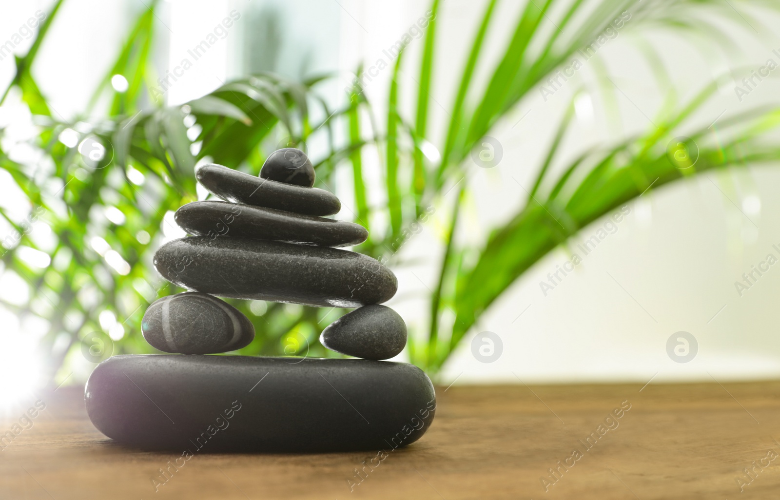 Photo of Table with stack of stones and blurred green leaves on background, space for text. Zen concept