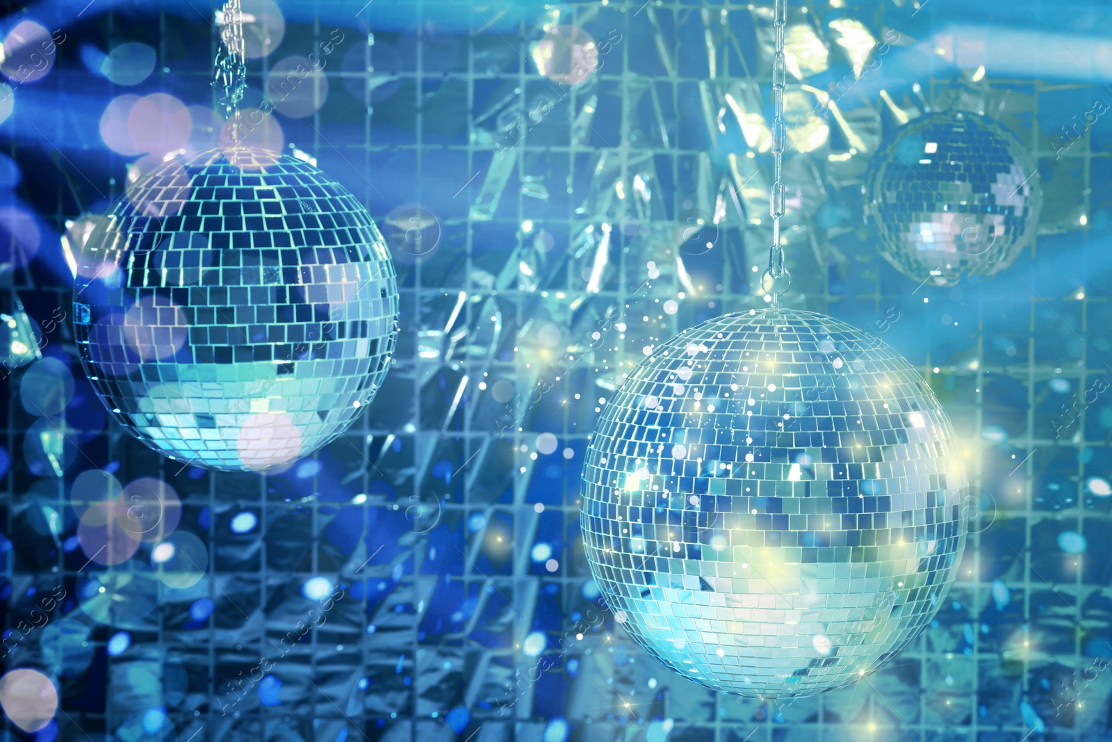 Image of Shiny disco balls against foil party curtain under blue lights, bokeh effect