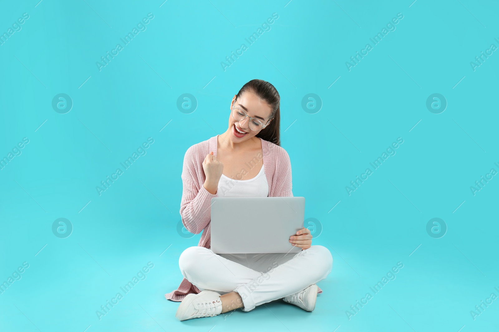 Photo of Happy young woman in casual outfit with laptop sitting on color background