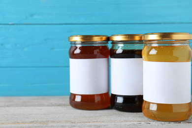 Photo of Jars of organic honey with blank labels on wooden table against light blue background. Space for text