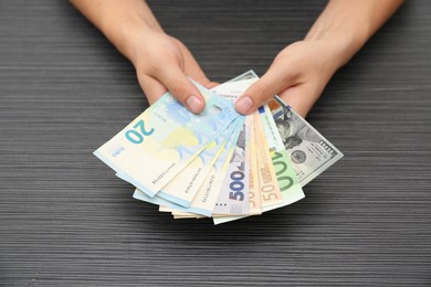 Currency exchange. Woman holding euro, hryvnia and dollar banknotes at wooden table, closeup