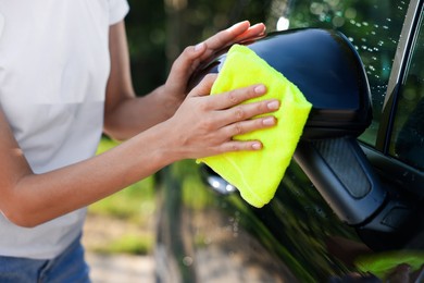 Photo of Woman washing car mirror with rag outdoors, closeup