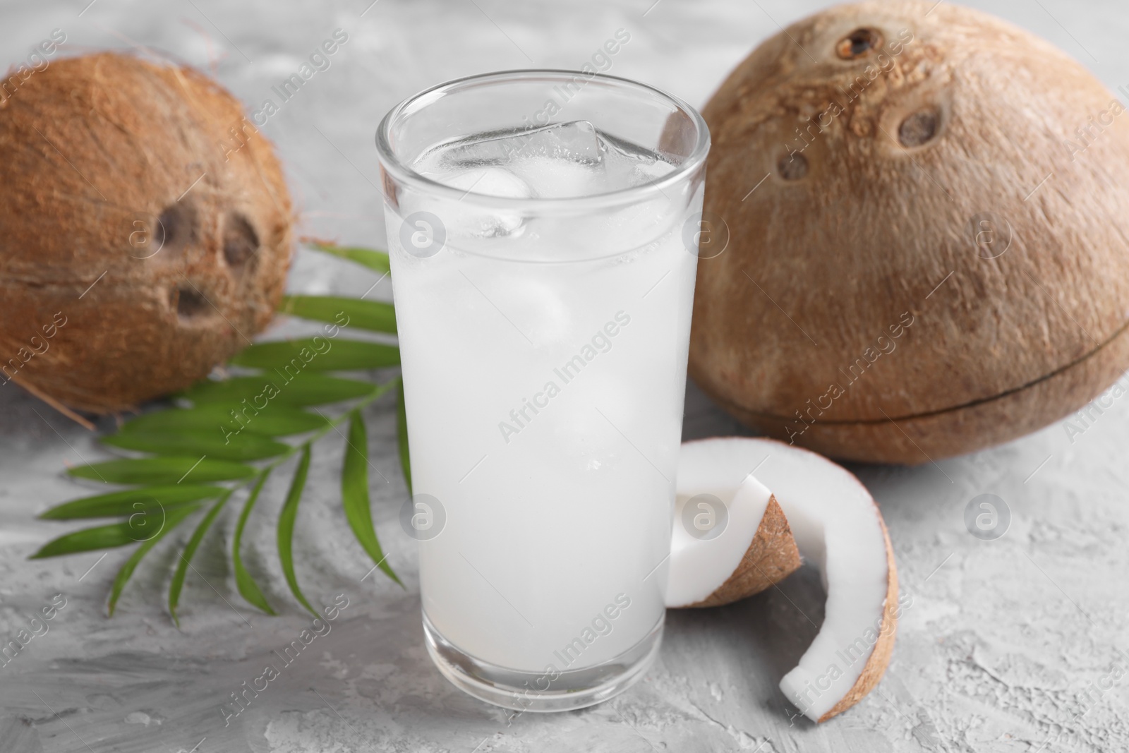 Photo of Glass of coconut water with ice cubes, palm leaf and nuts on grey table