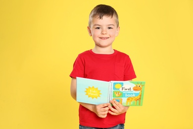 Cute little boy reading book on color background