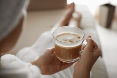 Photo of Woman with cup of hot drink on sofa at home in morning, closeup