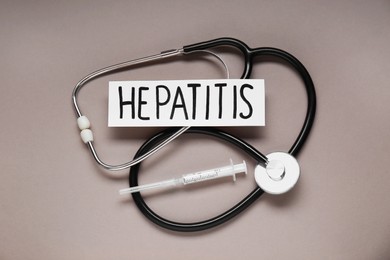 Photo of Word Hepatitis, stethoscope and syringe on beige background, flat lay