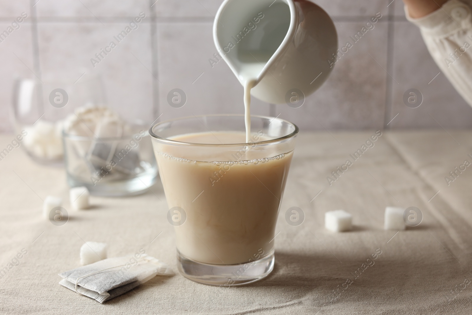 Photo of Pouring milk into cup with tea on light table, closeup