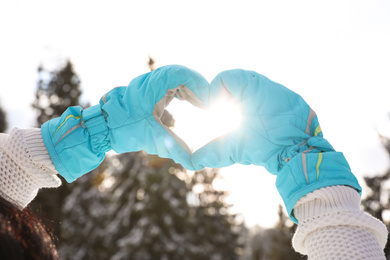 Photo of Young woman making heart with hands outdoors, closeup. Winter vacation