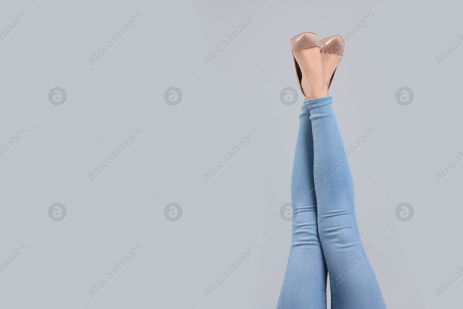 Photo of Woman wearing stylish jeans and high heels shoes on light gray background, closeup. Space for text