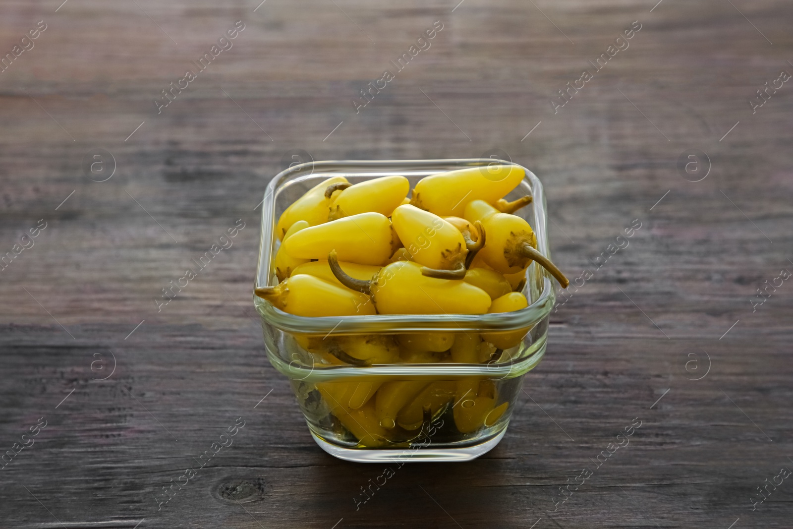 Photo of Glass bowl of pickled yellow jalapeno peppers on wooden table