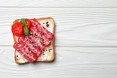 Photo of Tasty toast with slices of sausages, tomatoes and cream cheese on white wooden table, top view. Space for text