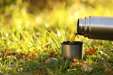 Photo of Pouring tea from thermos into cup lid on green grass outdoors, closeup. Space for text