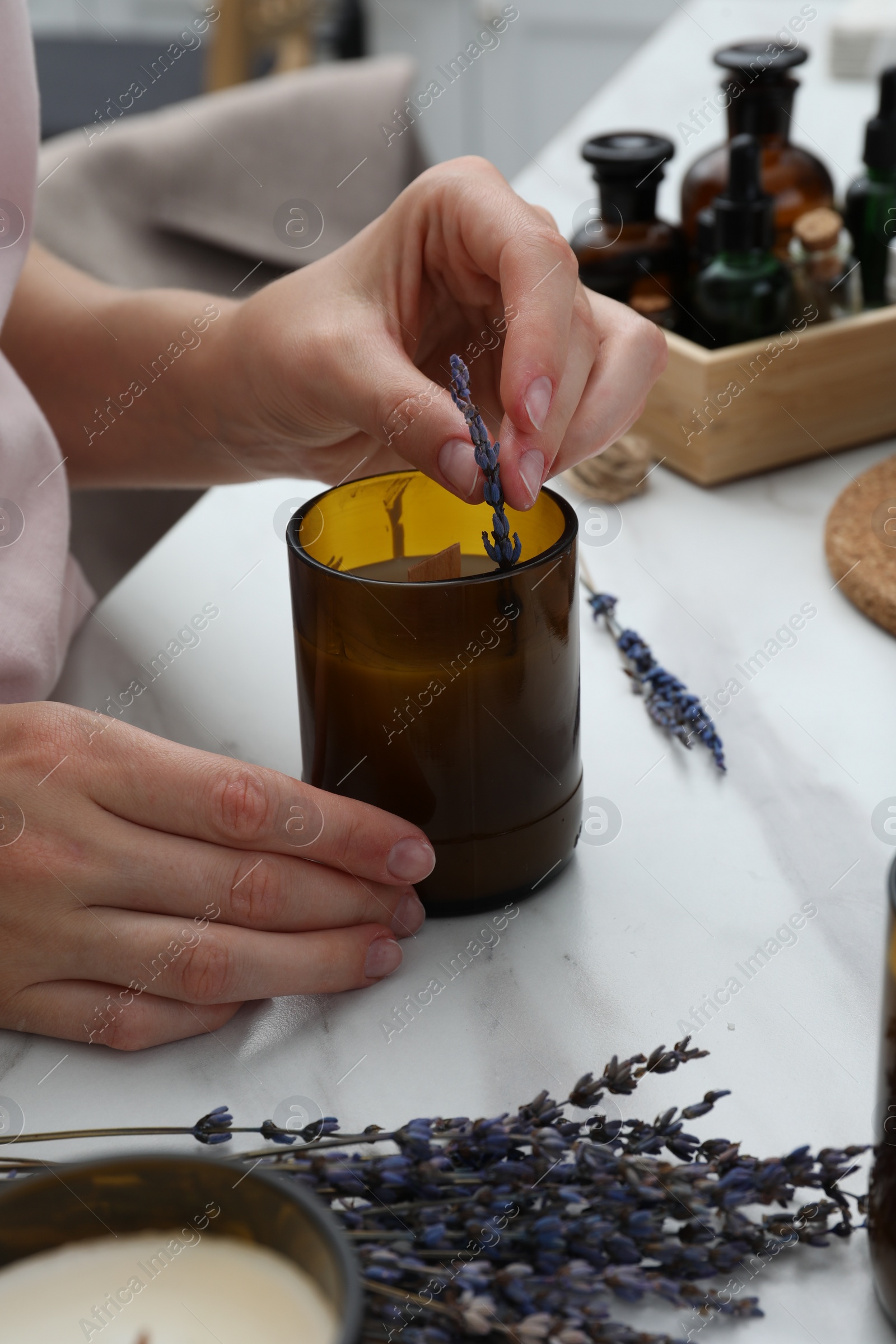 Photo of Woman decorating homemade candle with lavender flowers at table indoors, closeup