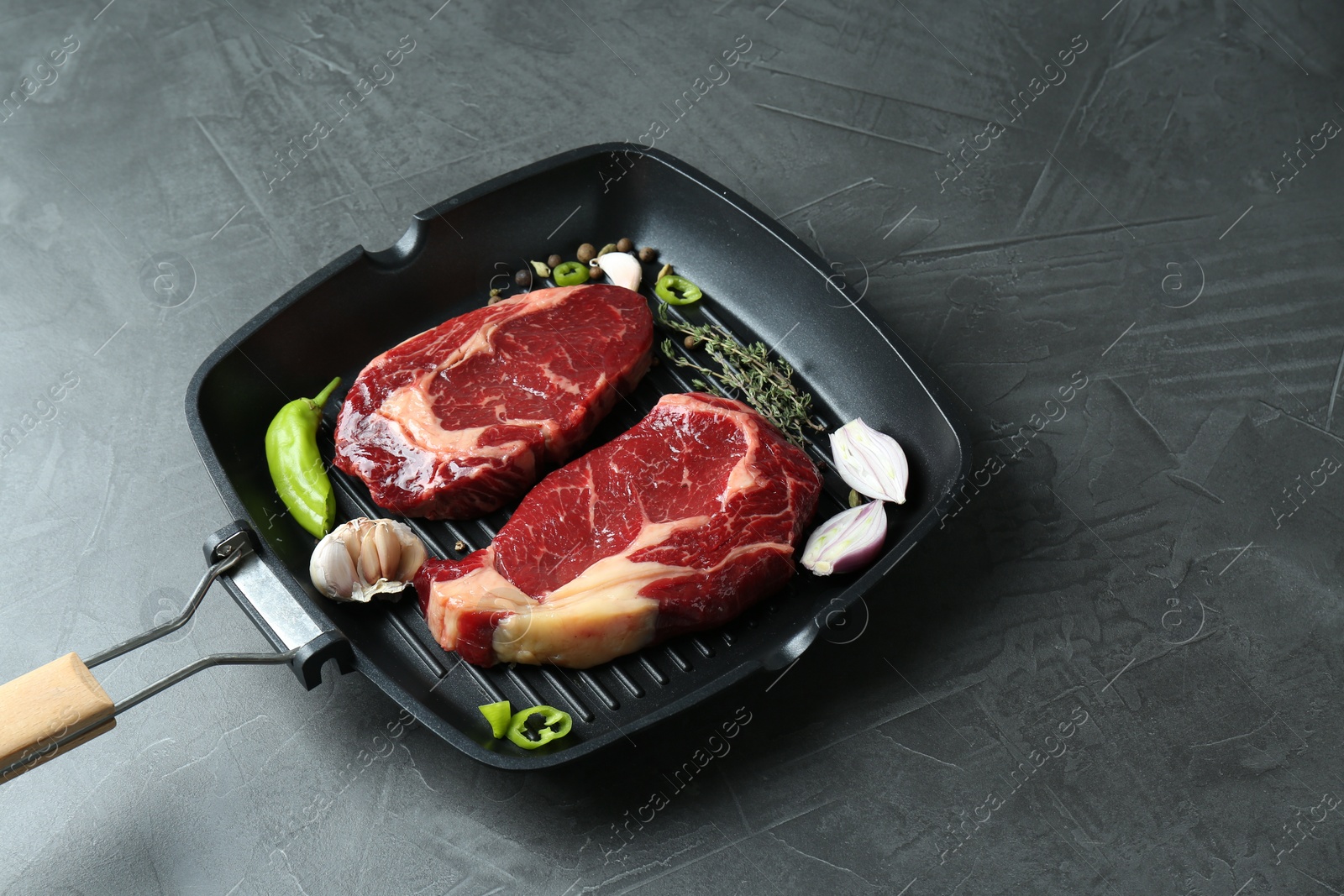 Photo of Grill pan with pieces of fresh beef meat, thyme and spices on gray table, space for text