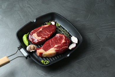 Grill pan with pieces of fresh beef meat, thyme and spices on gray table, space for text