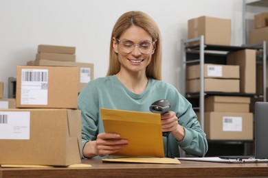 Photo of Seller with scanner reading parcel barcode at table in office. Online store