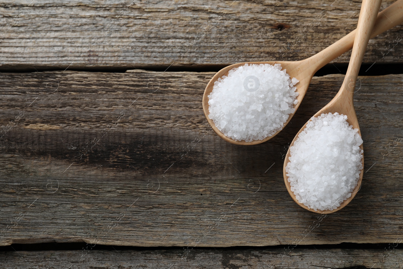 Photo of Organic salt in spoons on wooden table, flat lay. Space for text