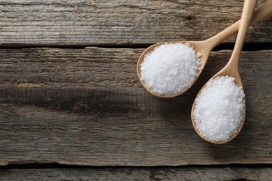 Photo of Organic salt in spoons on wooden table, flat lay. Space for text