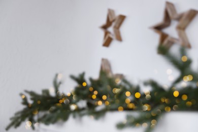 Blurred view of wooden stars and fir tree branches on white wall. Christmas decor