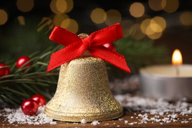 Photo of Bell with red bow and Christmas decor on wooden table against blurred background, closeup