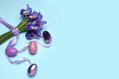 Photo of Beautiful iris flowers and painted eggs on light blue background, flat lay. Space for text