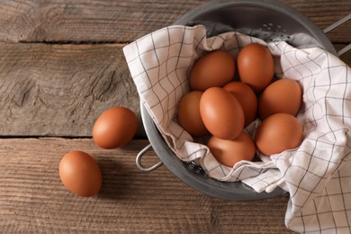 Chicken eggs in colander with napkin on wooden table, flat lay