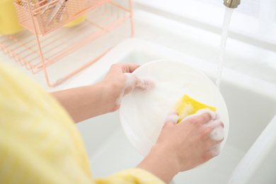 Photo of Woman washing ceramic plate in kitchen, closeup