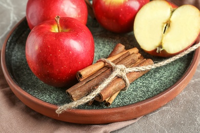 Photo of Fresh apples and cinnamon sticks on plate, closeup