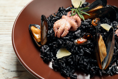 Delicious black risotto with seafood on white wooden table, closeup