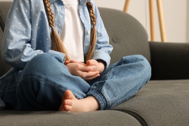 Photo of Little girl meditating on soft sofa indoors, closeup