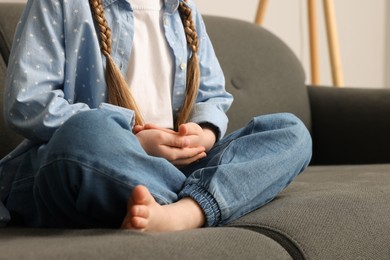 Little girl meditating on soft sofa indoors, closeup