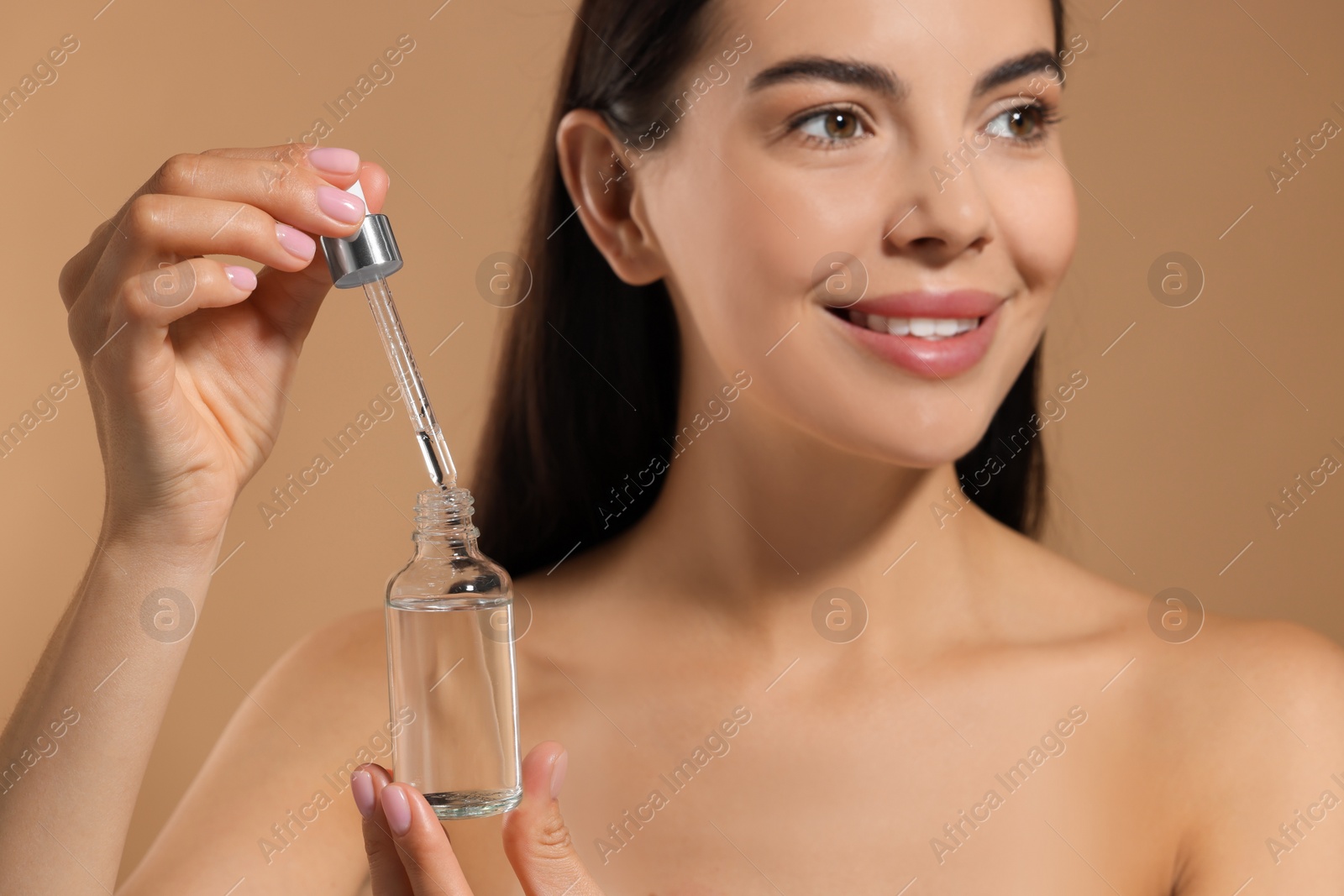 Photo of Beautiful young woman with serum in her hands on beige background, selective focus