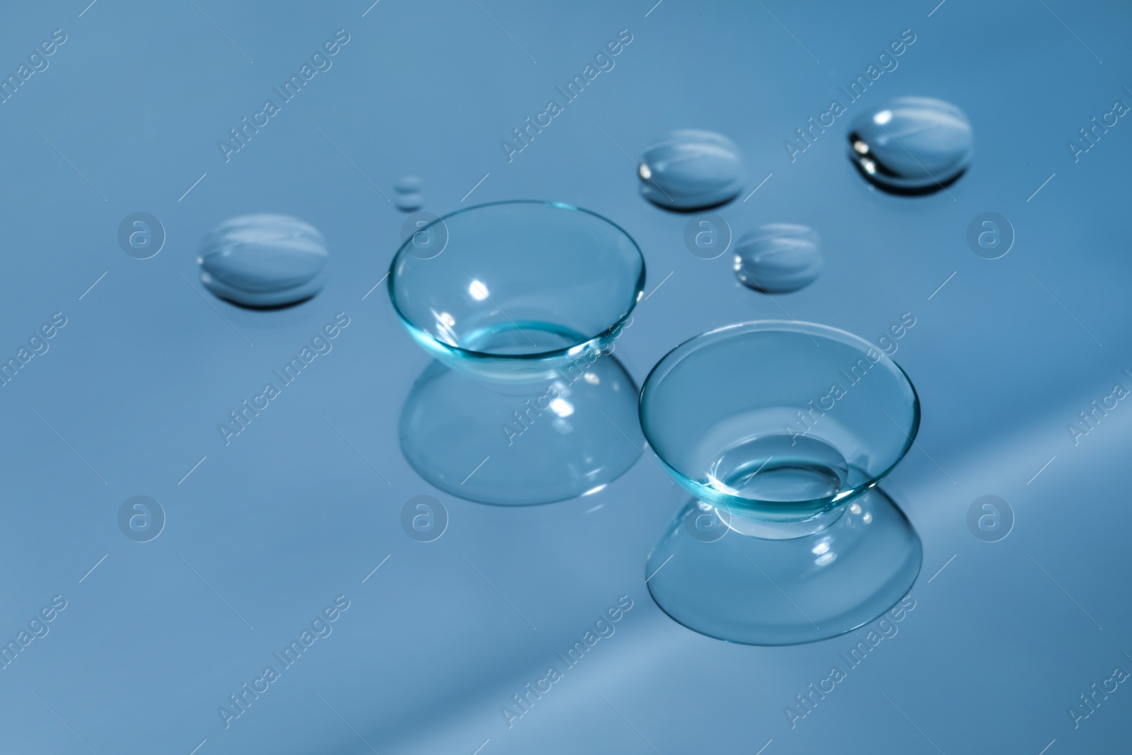 Photo of Contact lenses and drops of water on light blue reflective surface