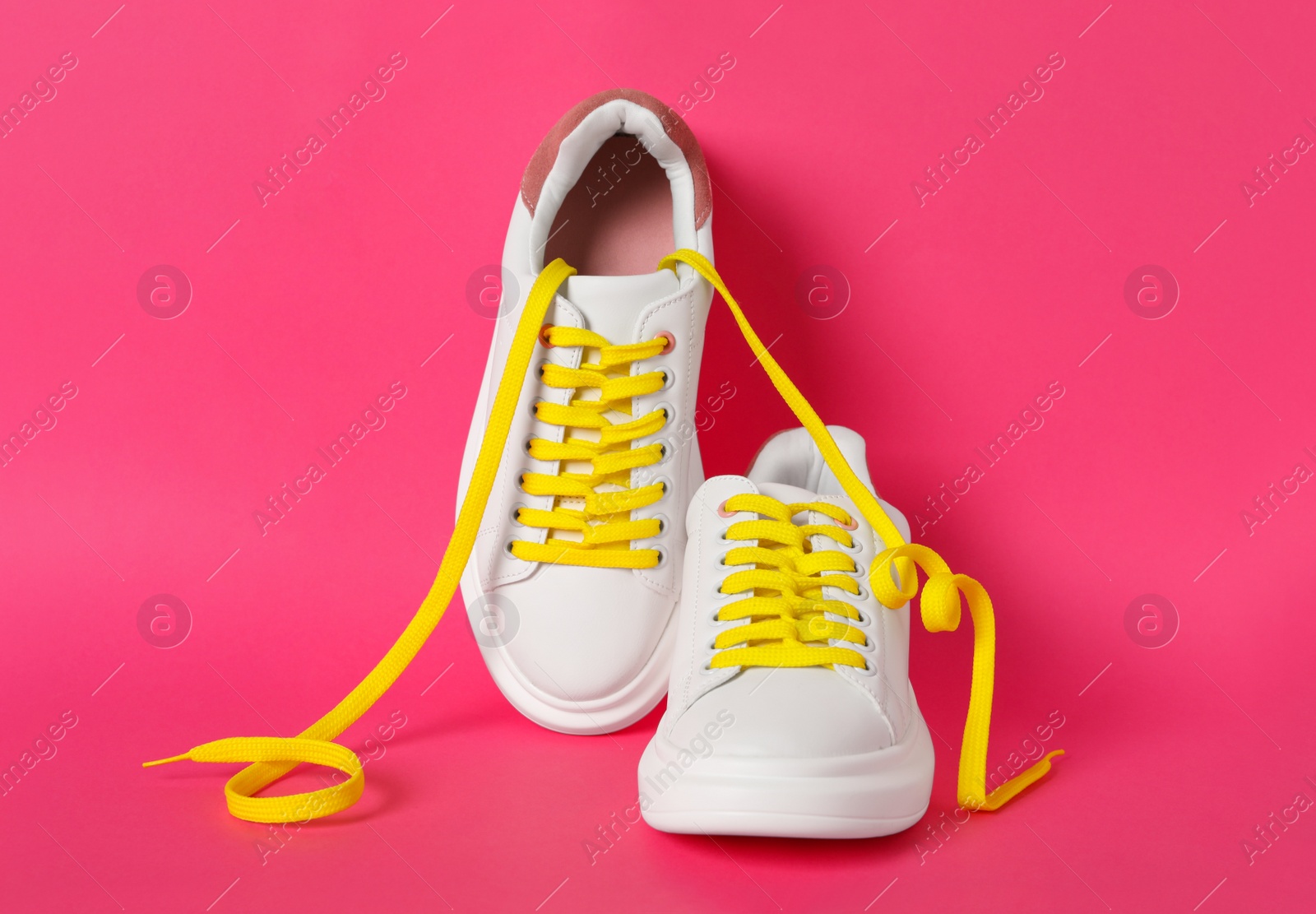 Photo of Pair of stylish shoes with yellow laces on pink background