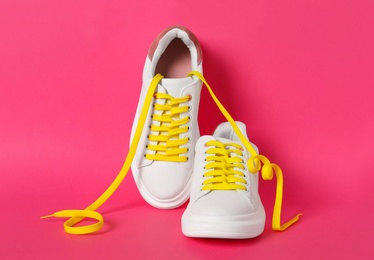 Pair of stylish shoes with yellow laces on pink background