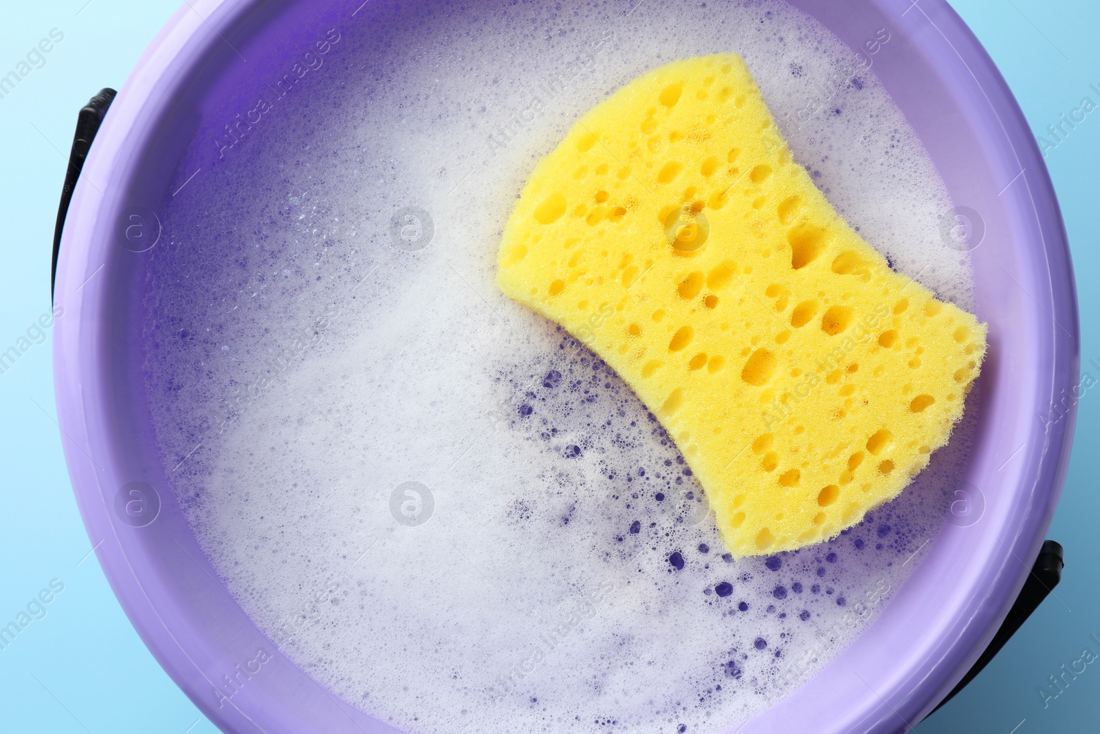 Photo of Bucket with foam and sponge on light blue background, top view