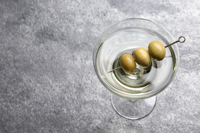 Photo of Martini cocktail with olives on grey table, above view. Space for text