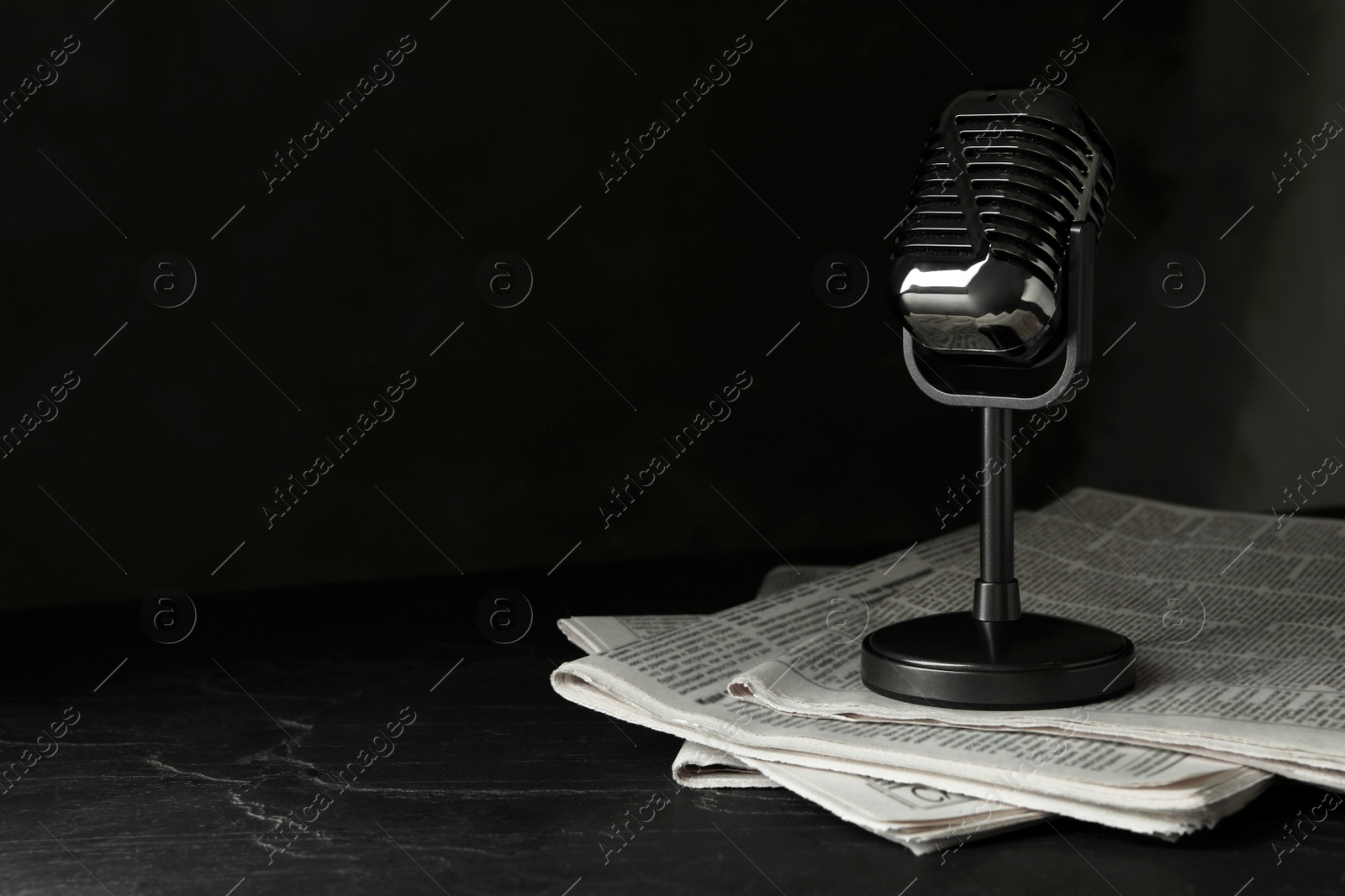 Photo of Newspapers and vintage microphone on dark stone table, space for text. Journalist's work